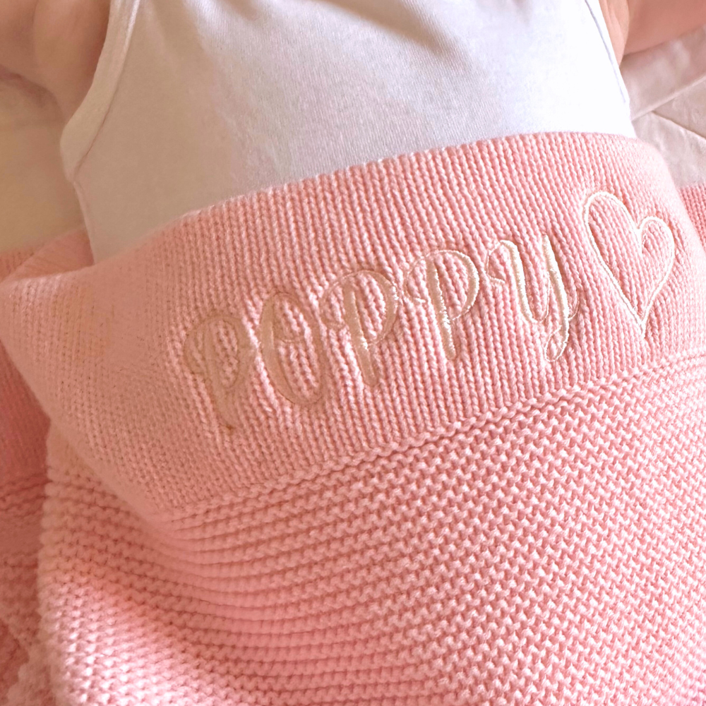 Close-up of a baby pink cotton knit baby blanket personalised & embroidered with the name 'Poppy' on it